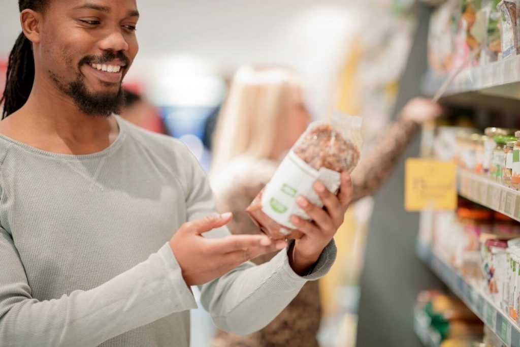A man with dreadlocks smiling as he reads the label on a food package
