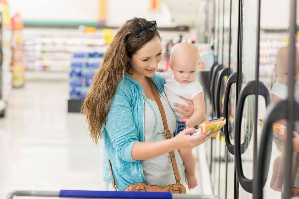 Mother holding a baby reading the label on the back of a packet of frozen vegetables