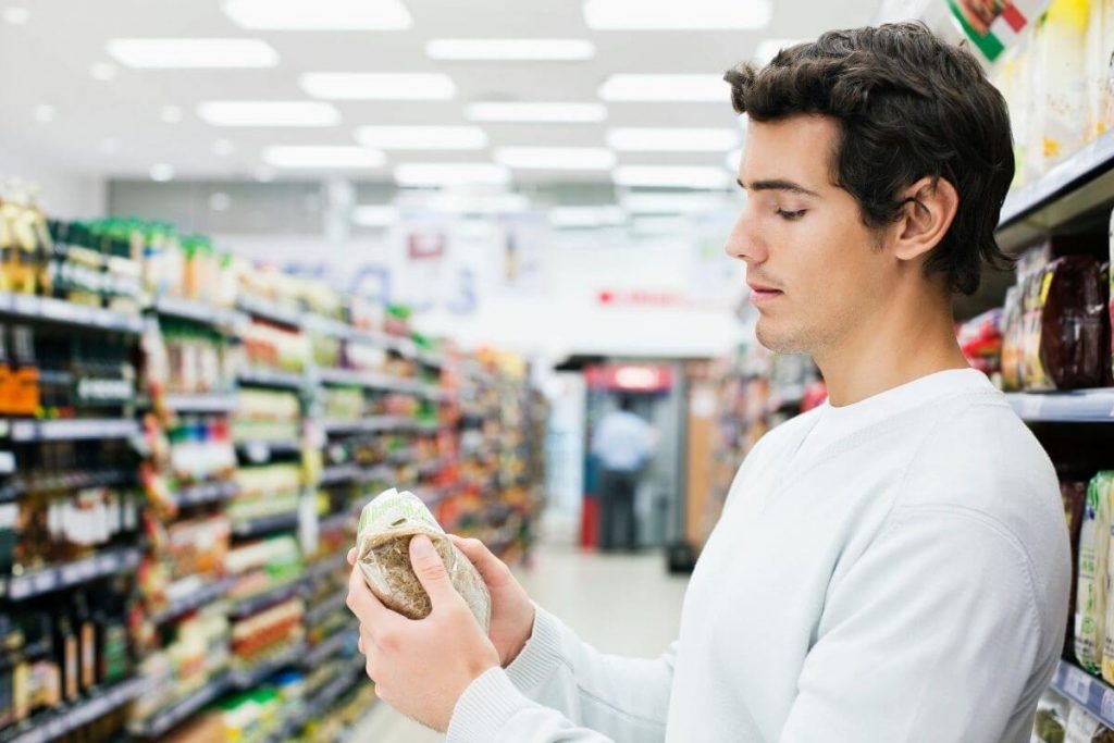 A young man reading the label on a food item in a supermarket