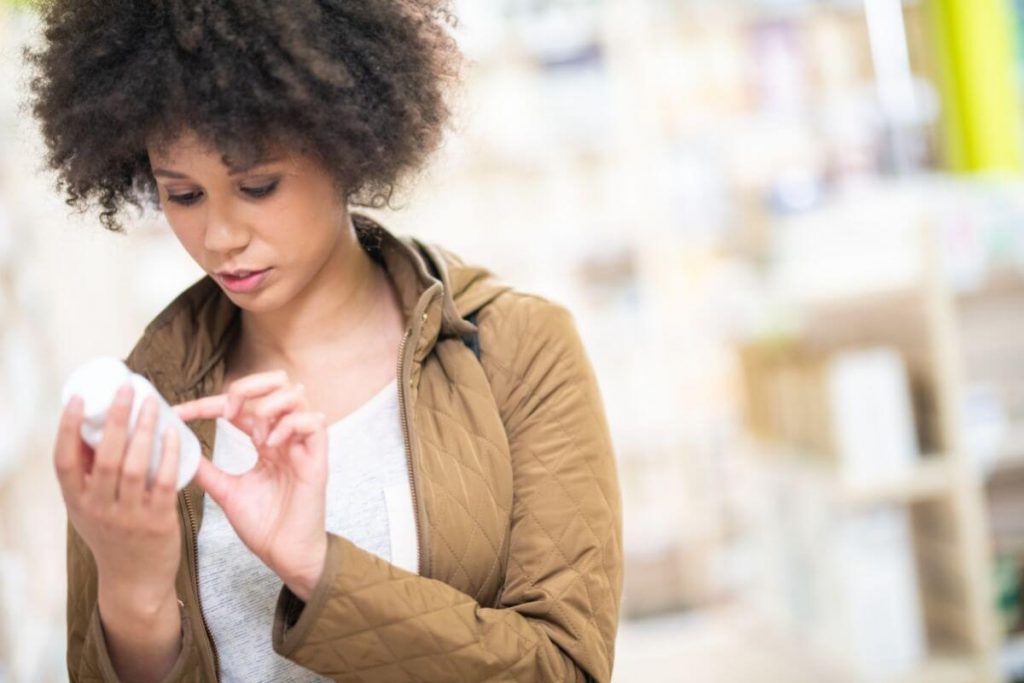 A young woman with an afro reading the ingredients on a bottle of supplements
